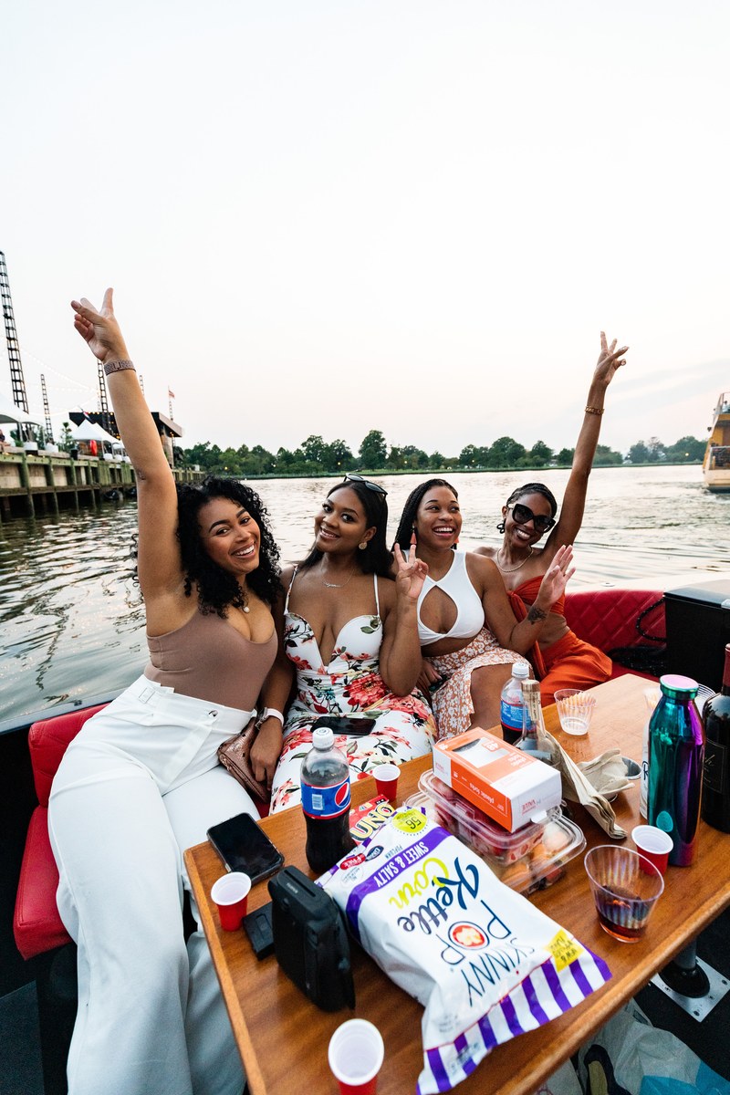 Four friends celebrating with peace signs around a snack-filled table on a private Yachtsy cruise at sunset