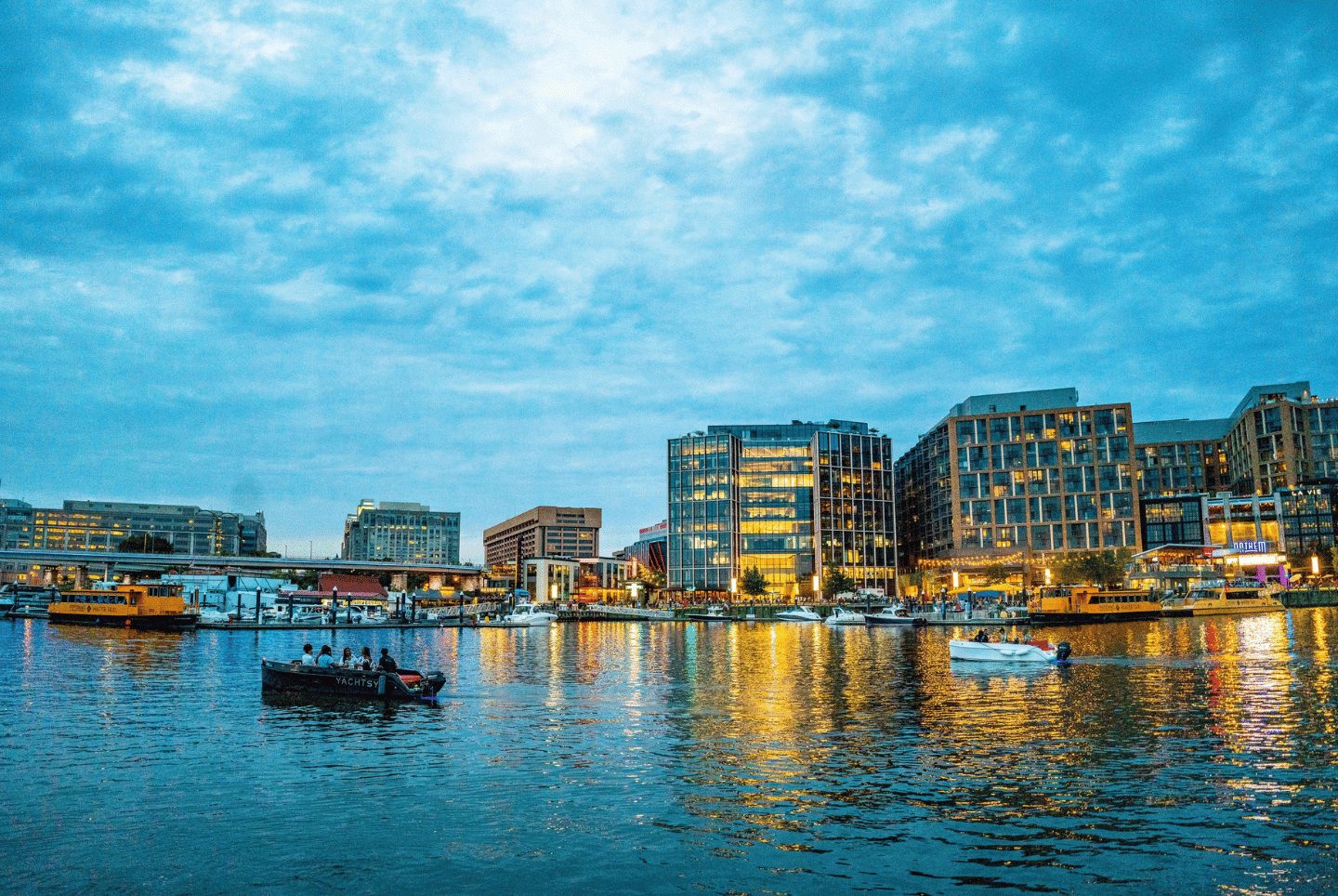 Guests aboard a Yachtsy boat cruising past a city waterfront glowing at dusk