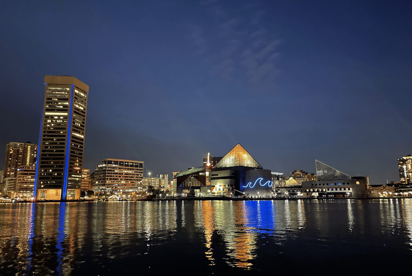 Baltimore's Inner Harbor skyline and National Aquarium lit up at night, reflected on the water